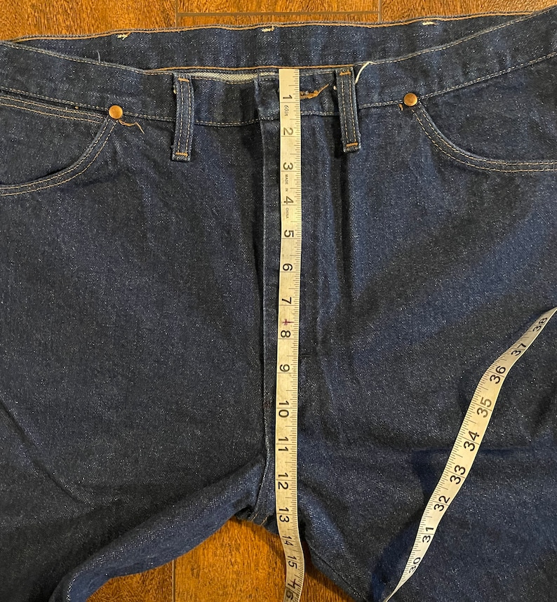 Puede incluir: Un par de pantalones vaqueros de mezclilla azul oscuro con una cinta m&eacute;trica que corre verticalmente por la costura central. La cinta mide 40,6 cm.