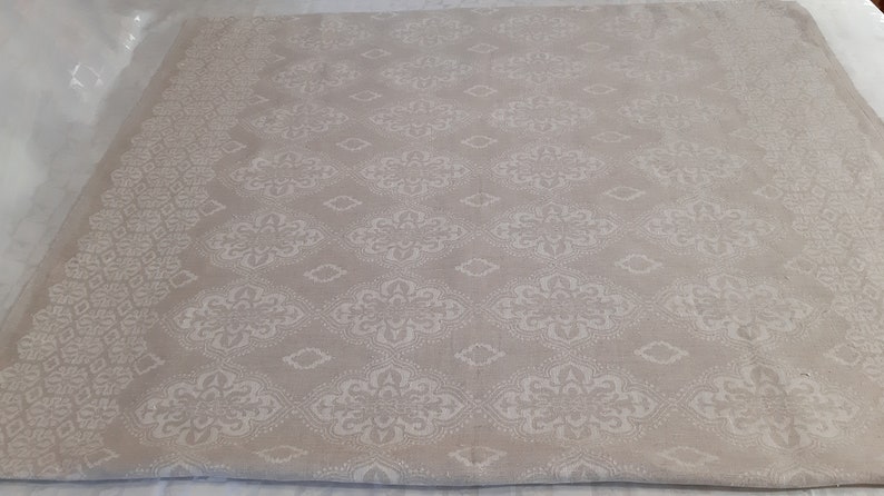 May include: A beige fabric with a white damask pattern. The fabric has a subtle sheen and a soft texture.