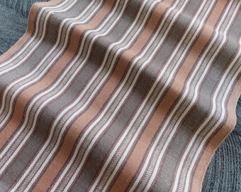 May include: A striped fabric with brown and orange stripes. The fabric has a woven texture and is folded in half.
