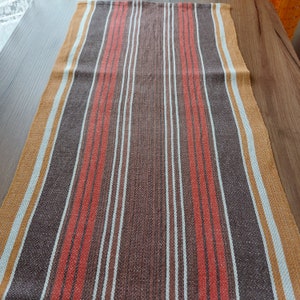 May include: A striped table runner with brown, orange, and white stripes. The runner is made of a woven fabric and has a textured surface.