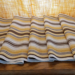 May include: Five brown, white, and yellow striped fabric table runners. The runners are folded and laid out on a wooden surface.