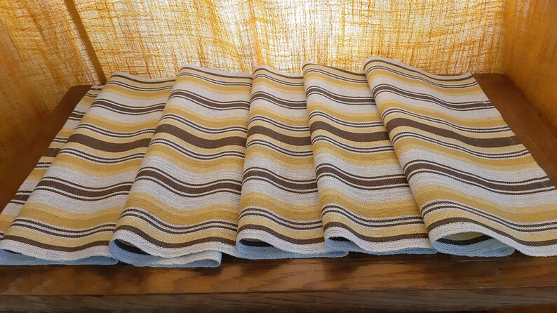 May include: Five brown, white, and yellow striped fabric table runners. The runners are folded and laid out on a wooden surface.