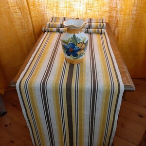 May include: A yellow, brown, and white striped table runner with a ceramic vase with floral designs on it.