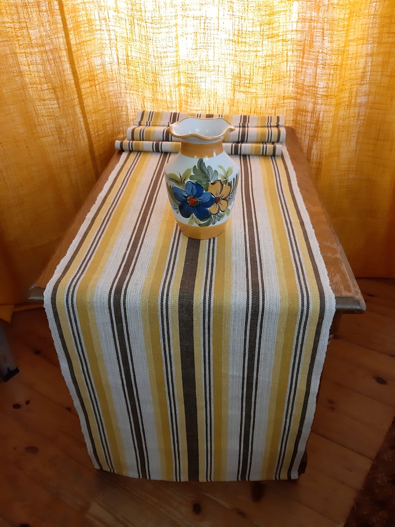 May include: A yellow, brown, and white striped table runner with a ceramic vase with floral designs on it.