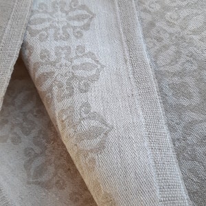 May include: Close-up of three white linen tea towels with a subtle embossed floral pattern. The towels are folded and stacked on top of each other.