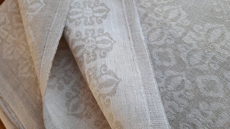 May include: Close-up of three white linen tea towels with a subtle embossed floral pattern. The towels are folded and stacked on top of each other.