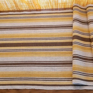May include: A striped table runner in brown, beige, and white. The runner is folded in thirds and is made of a woven fabric.