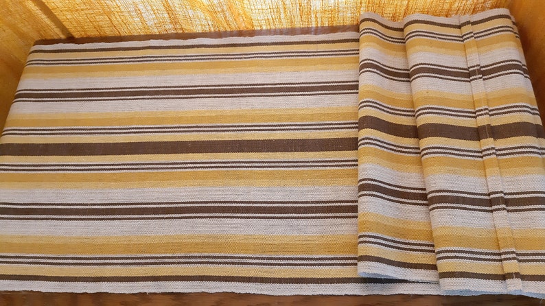 May include: A striped table runner in brown, beige, and white. The runner is folded in thirds and is made of a woven fabric.