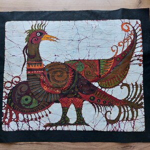 May include: A batik wall hanging featuring a stylized bird with intricate patterns in shades of red, brown, green, and gold. The bird has a long, curved neck and a large, detailed tail.