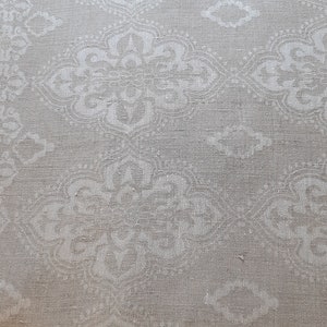 May include: A close-up of a white fabric with a subtle, embossed pattern of repeating floral designs. The fabric has a slightly textured, linen-like appearance.