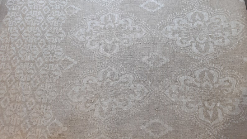 May include: A close-up of a white fabric with a subtle, embossed pattern of repeating floral designs. The fabric has a slightly textured, linen-like appearance.