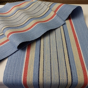 May include: A blue and white striped table runner with red stripes. The runner is made of a woven fabric and has a subtle texture.