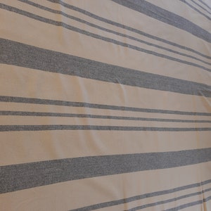 May include: A beige and gray striped fabric with a subtle texture. The fabric has a horizontal stripe pattern with alternating beige and gray stripes.