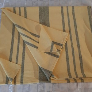 May include: A yellow and gray striped throw blanket folded on a white surface. The blanket has a woven texture and is made of a soft material.
