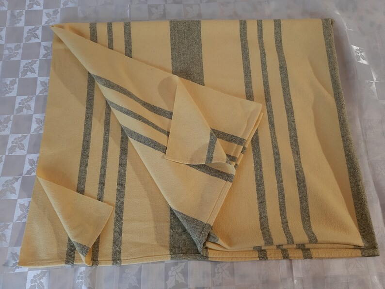 May include: A yellow and gray striped throw blanket folded on a white surface. The blanket has a woven texture and is made of a soft material.