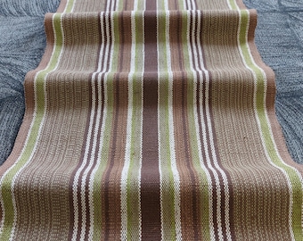 May include: A brown, green and white striped fabric runner. The runner is woven with a textured pattern and has a slightly distressed look.