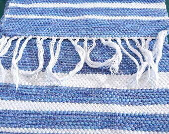 May include: A blue and white striped woven rug with white fringe. The rug is made of a thick, textured material.
