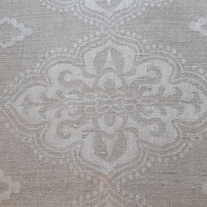 May include: A close-up of a white fabric with a subtle, repeating pattern of white floral designs. The fabric has a slightly textured surface.