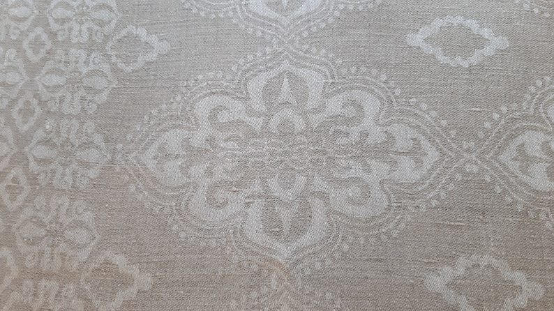 May include: A close-up of a white fabric with a subtle, repeating pattern of white floral designs. The fabric has a slightly textured surface.