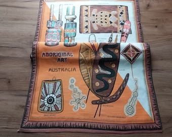 Op de afbeelding: Een kleurrijk stoffen paneel met illustraties van Aboriginal kunst uit Australië. Het paneel toont afbeeldingen van gedecoreerde speren, schilden, een boemerang, een schorsmand en grondtekeningen. De tekst "ABORIGINAL ART AUSTRALIA" is op het paneel gedrukt.
