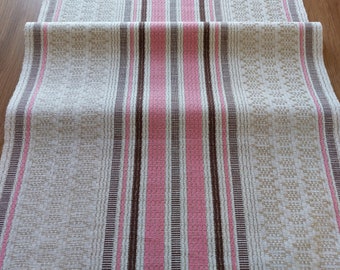 May include: A beige table runner with pink and brown stripes. The runner has a woven texture and a subtle pattern.
