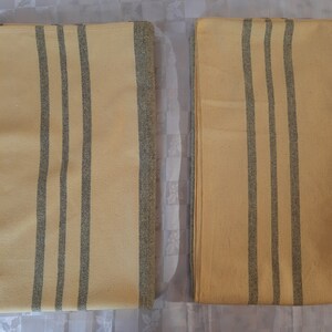 May include: Two yellow and gray striped blankets folded on a white surface. The blankets have a subtle texture and are made of a soft material.