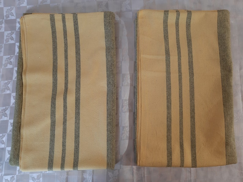 May include: Two yellow and gray striped blankets folded on a white surface. The blankets have a subtle texture and are made of a soft material.