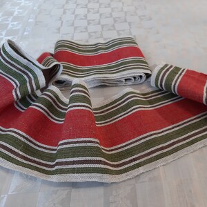 May include: Several pieces of woven fabric with a red central stripe, bordered by green and white stripes. The fabric is folded and rolled, with a frayed edge visible on some pieces. The overall theme is home textiles.