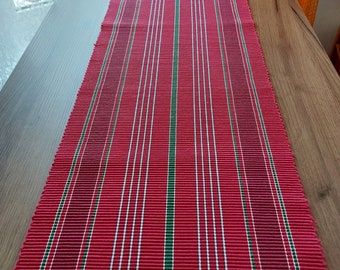 May include: Red and green striped table runner with a woven texture. The runner is made of a fabric material and has a rectangular shape.