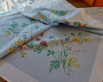 May include: A light blue tablecloth with a floral pattern featuring yellow, red, green, and blue flowers. The tablecloth has a white border.