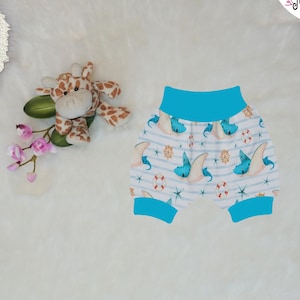 Könnte beinhalten: Türkisblaue Baby-Blümchen mit weißem Hintergrund und einem maritimen Muster aus blauen Rochen, Sternen, Ankern und roten Rettungsringen. Der Text "Bündchen "Türkis-Blau"" ist unter den Blümchen gedruckt.