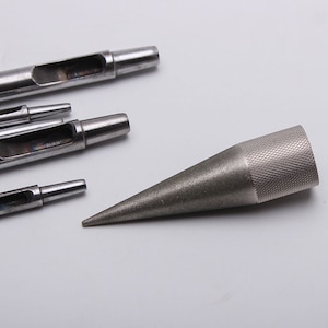 May include: A set of metal leather hole punches and a metal awl with a pointed tip. The punches are of different sizes and have a hollow center. The awl is used for making holes in leather.