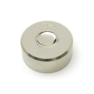 May include: A silver metal round die with a recessed center and the word "SEKIWA" engraved on the top.