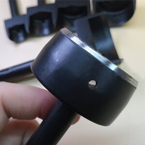 May include: A close-up of a black leather punch tool with a round, beveled edge and a small hole in the center. The tool is used for creating holes in leather for stitching or other decorative purposes.