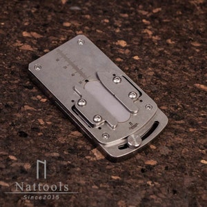 May include: A silver metal multi-tool with a ruler, a blade, and a small screwdriver. The tool is folded closed and has a small knob on the side.