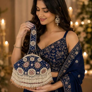 May include: A navy blue handbag featuring intricate embroidery with white and pink floral patterns, accented by a top handle and a decorative fringe of white pearls and small beads hanging from the bottom edge of the structured frame.