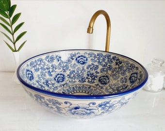 Könnte beinhalten: Ein weißes Keramikwaschbecken mit einem blauen und weißen Blumenmuster. Das Waschbecken ist rund und hat einen goldenen Wasserhahn.