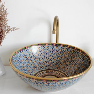 May include: A blue and gold ceramic sink with a floral pattern. The sink is round and has a wide rim. The sink is on a white countertop.