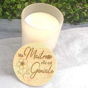 May include: A white frosted glass candle jar with a wooden lid. The lid has a floral design and the text "Ma Maitresse elle est Geniale".