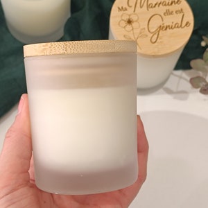 May include: A frosted glass candle jar with a bamboo lid. The lid has the text "Ma Marraine elle est Geniale" engraved on it.
