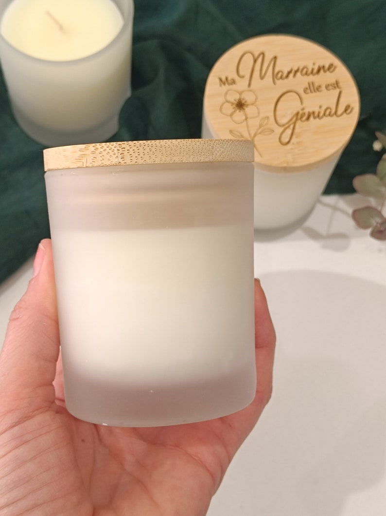 May include: A frosted glass candle jar with a bamboo lid. The lid has the text "Ma Marraine elle est Geniale" engraved on it.
