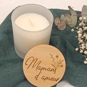 May include: A frosted glass candle with a wooden lid. The lid has the text "Maman d'amour" engraved on it with a floral design.