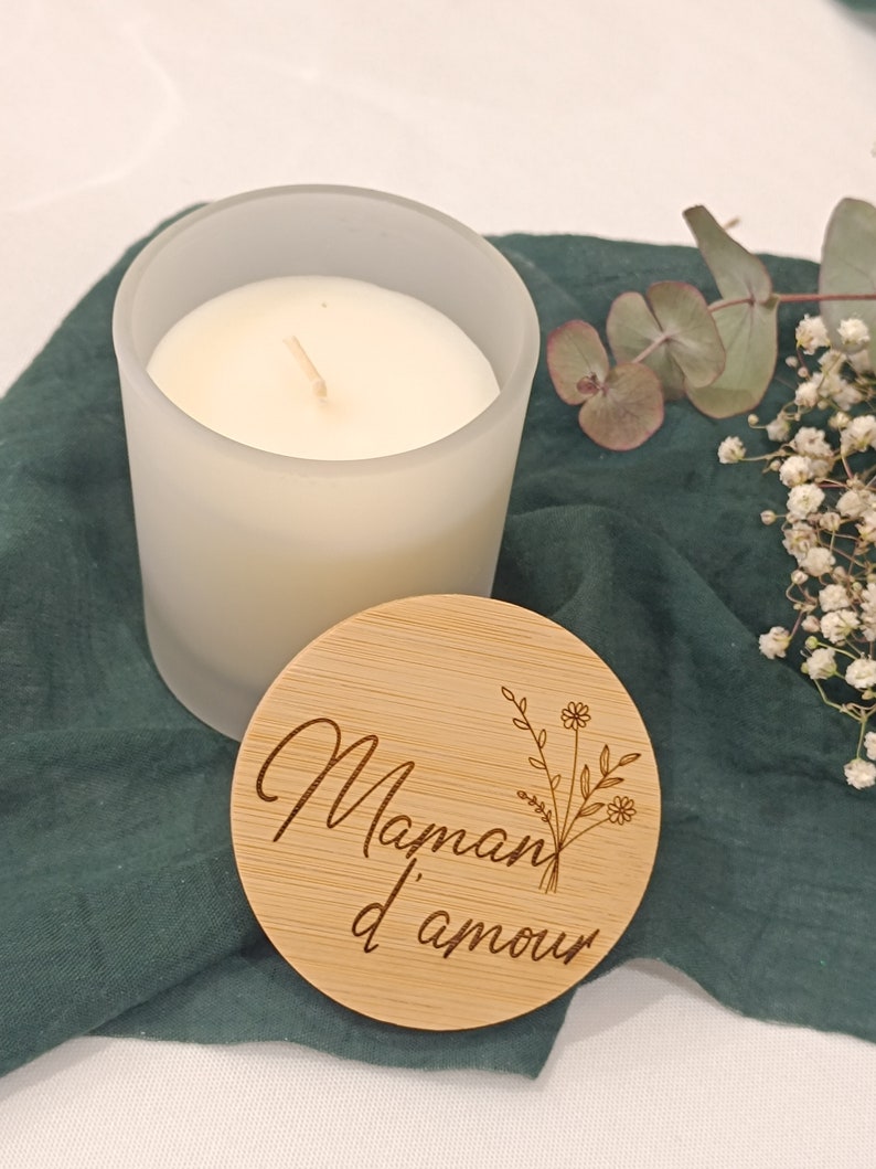 May include: A frosted glass candle with a wooden lid. The lid has the text "Maman d'amour" engraved on it with a floral design.