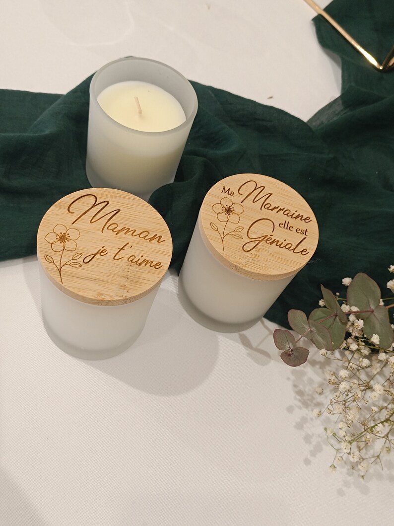 May include: Two white frosted glass candle jars with wooden lids. The lids are engraved with the text "Maman je t'aime" and "Ma Marraine elle est Geniale".