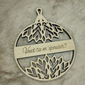 Puede incluir: Un adorno navideño de madera con forma de círculo con un diseño decorativo y el texto "Veux tu m'épouser?" que se traduce como "¿Te quieres casar conmigo?" en español.