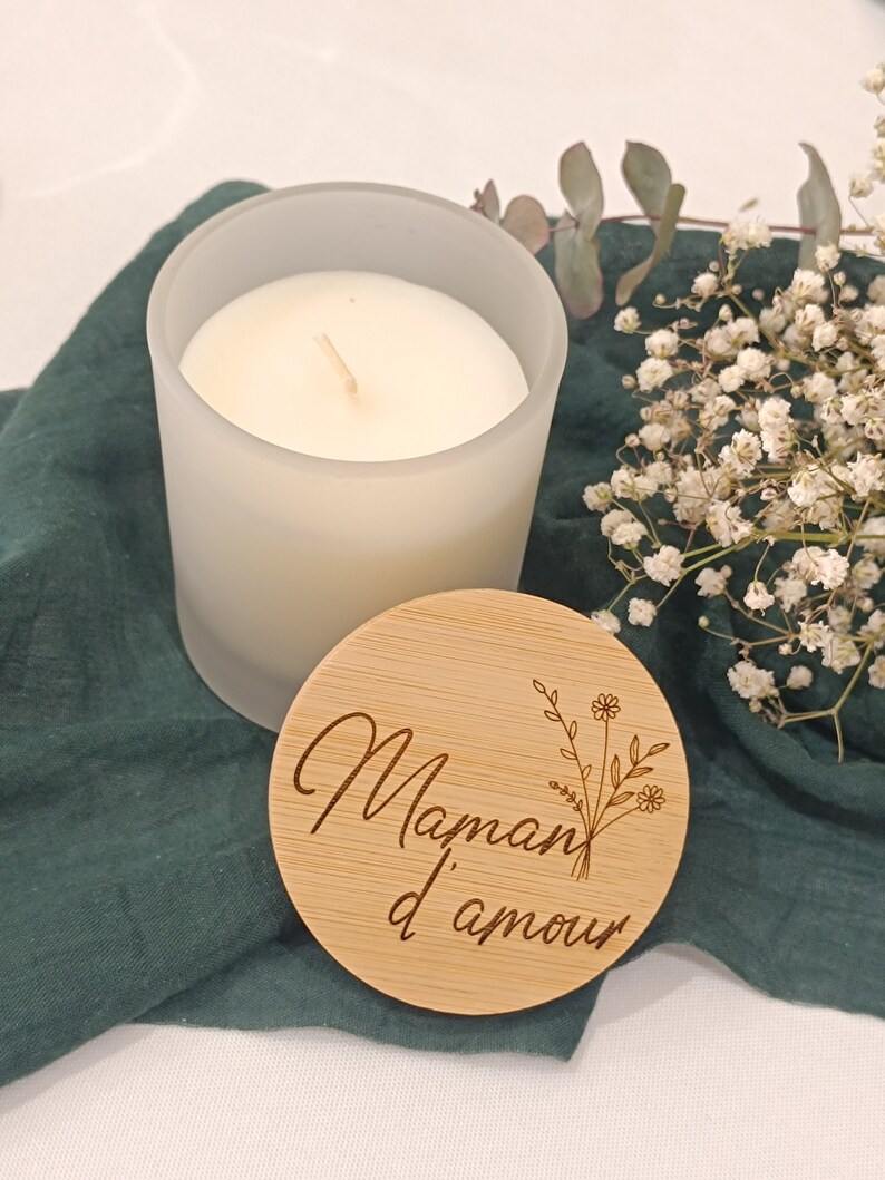 May include: A white frosted glass candle with a wooden lid. The lid is engraved with the text "Maman d'amour" and a floral design.