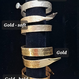 May include: Four hammered metal bracelets stacked on a black display stand. The bracelets are in three different finishes: champagne, gold, and gold - soft. The bracelets are all the same width and have a slightly curved shape.