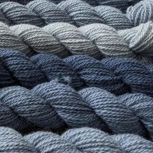 May include: A collection of skeins of yarn in various shades of blue, from light to dark, arranged in a staggered pattern.