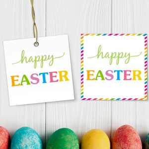 May include: Two printable Easter gift tags with the text "happy easter" in colourful letters. The tags are on a white wood background with colourful Easter eggs in the foreground.