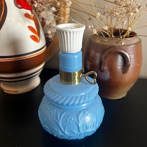 Könnte beinhalten: Ein hellblauer Öllampensockel aus Glas mit einem geformten Blumenmuster und einem gedrehten Seildesign um die Schulter. Er enthält einen messingfarbenen Metallkragen mit einem kleinen herzförmigen Griff und einen weißen geriffelten Brenner.